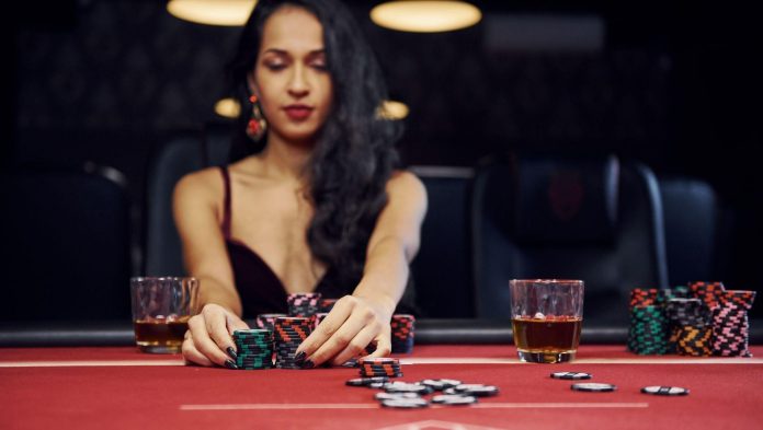 Woman in elegant clothes sits in cassino by table and plays poker game Pro Photo